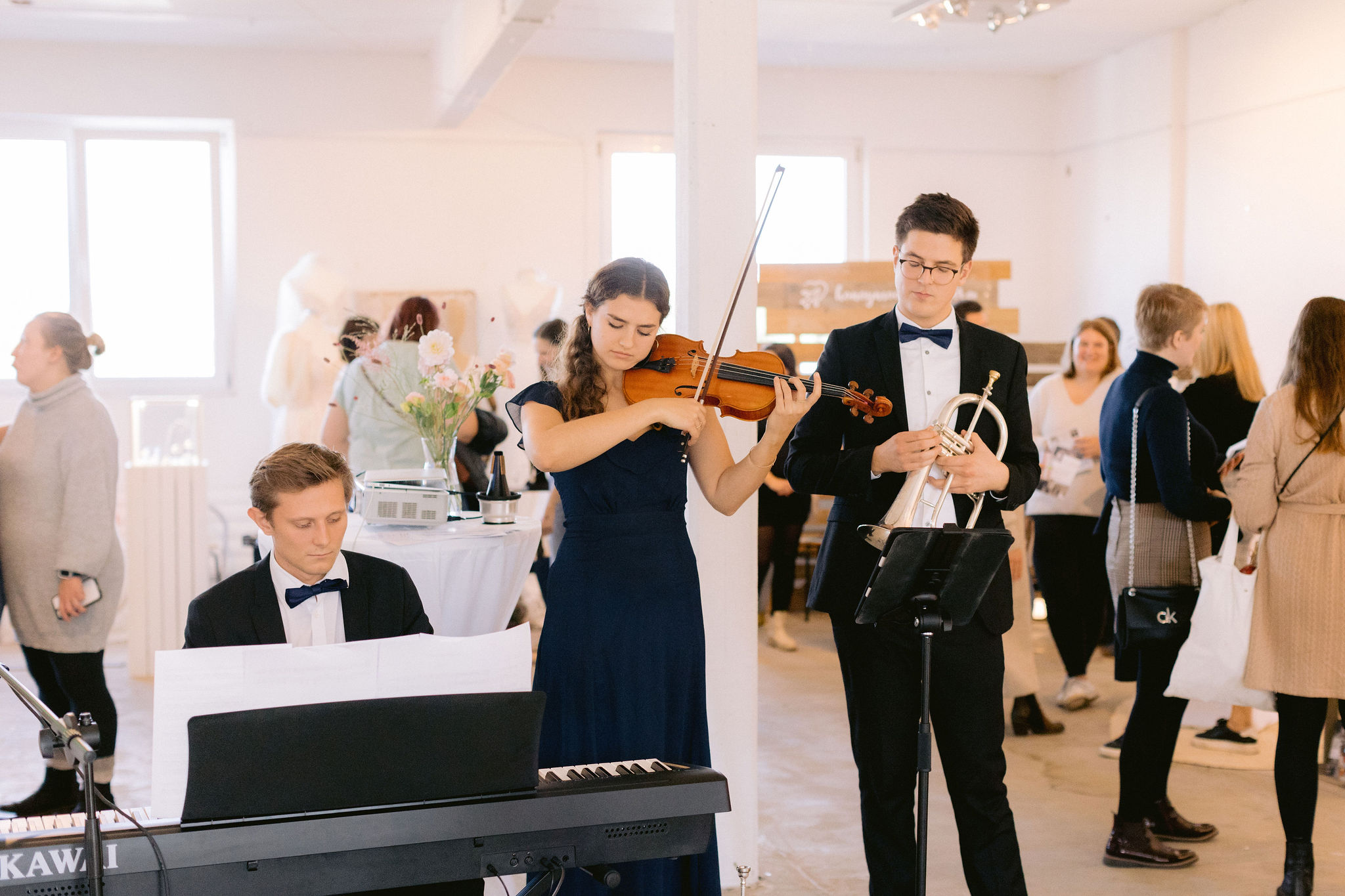 Ein Musiktrio. Ein Mann spielt Klavier, eine Frau Geige und ein weiterer Mann Trompete.